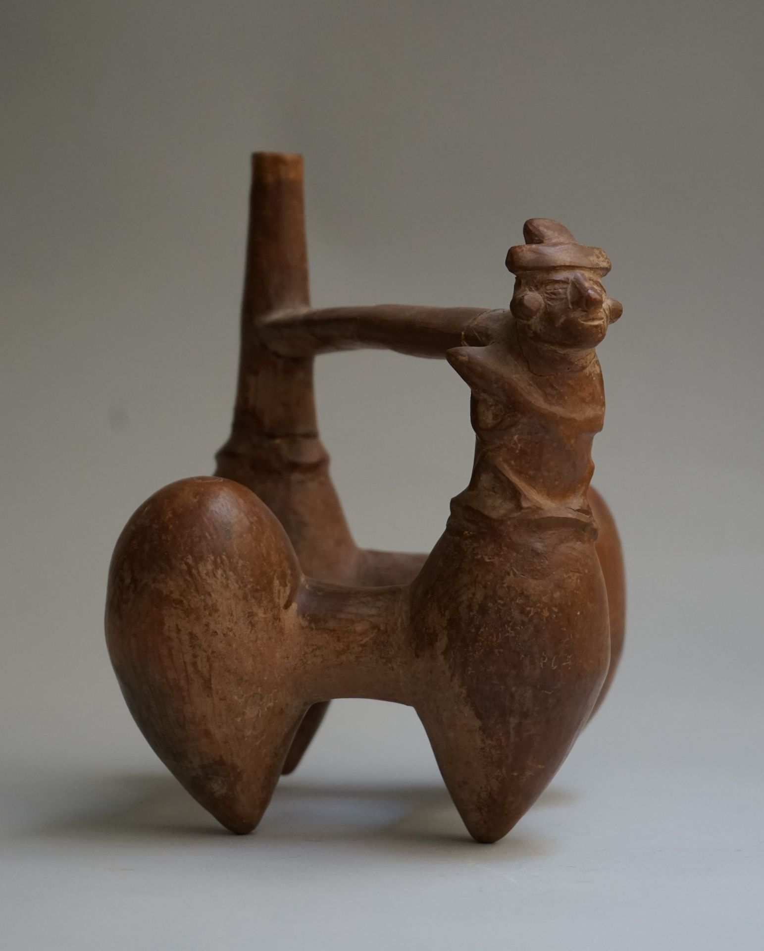 Null 吹口哨的花瓶，有四个水果形的脚，其中一个脚上有一个手持棍棒的人物，通过一个桥形把手与瓶身相连。橙色-米色的陶土。手柄和颈部破损并被粘住。

兰巴耶克，&hellip;