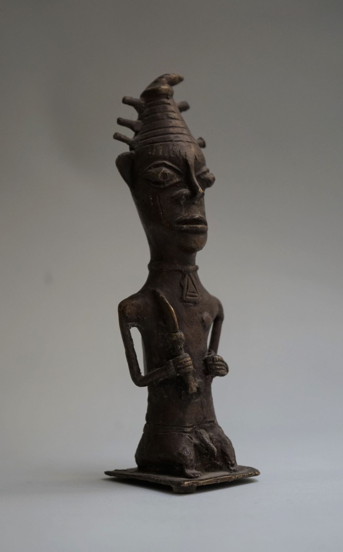 Null 拟人化的巫师雕像，手持祭祀用品，头上戴着带有突起的圆锥形帽子。青铜，带有棕色的铜锈。

刚果民主共和国。

高：21厘米