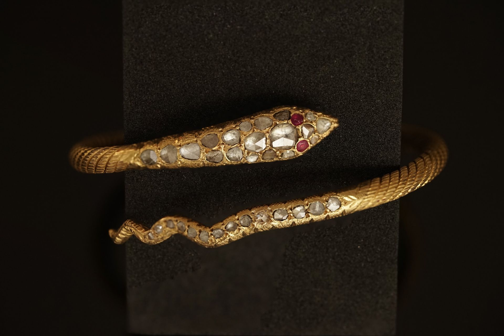 Null 18K(750/°)黄金手镯，形成一条蛇的开放式带子，蛇头和蛇尾装饰着玫瑰，眼睛是红宝石。20世纪初。PB：47.11g