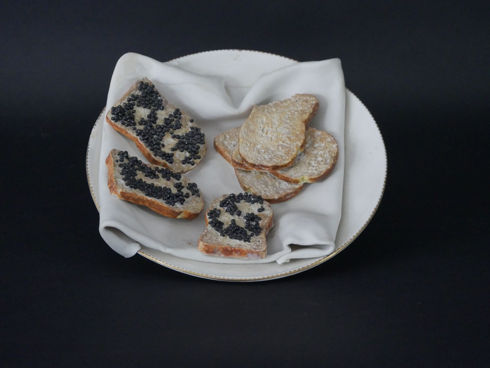 ASSIETTE en faïence fine à décor de toasts beurrés et caviar posé sur un linge. &hellip;