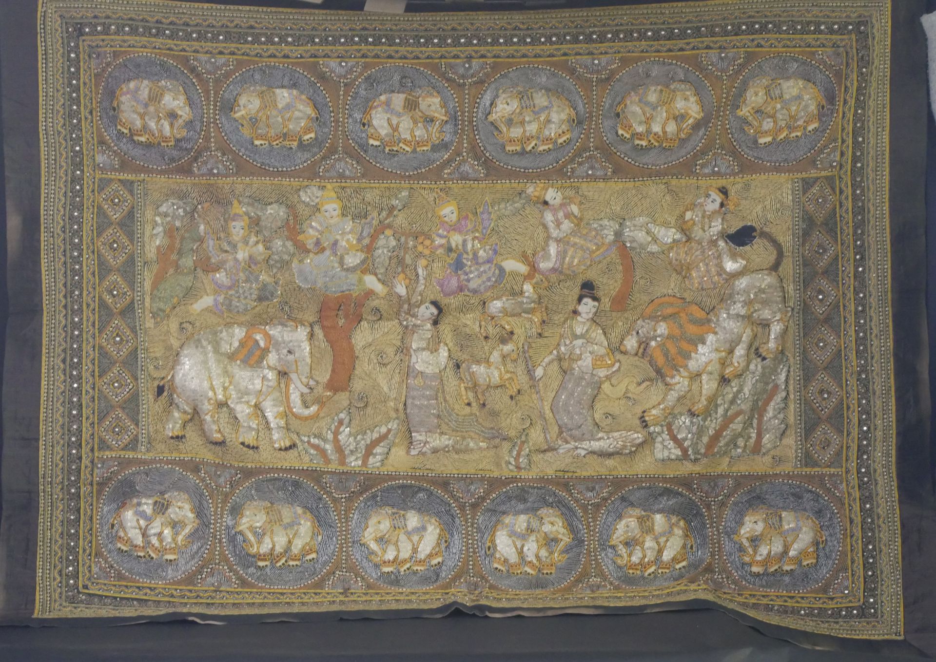 Null 丝绸、银线和坎尼特线装饰，描绘了宫廷女官、大象、狮子和跳舞的女孩。两块表现大象的奖章楣板。20世纪的印度尼西亚作品。140 x 175厘米。