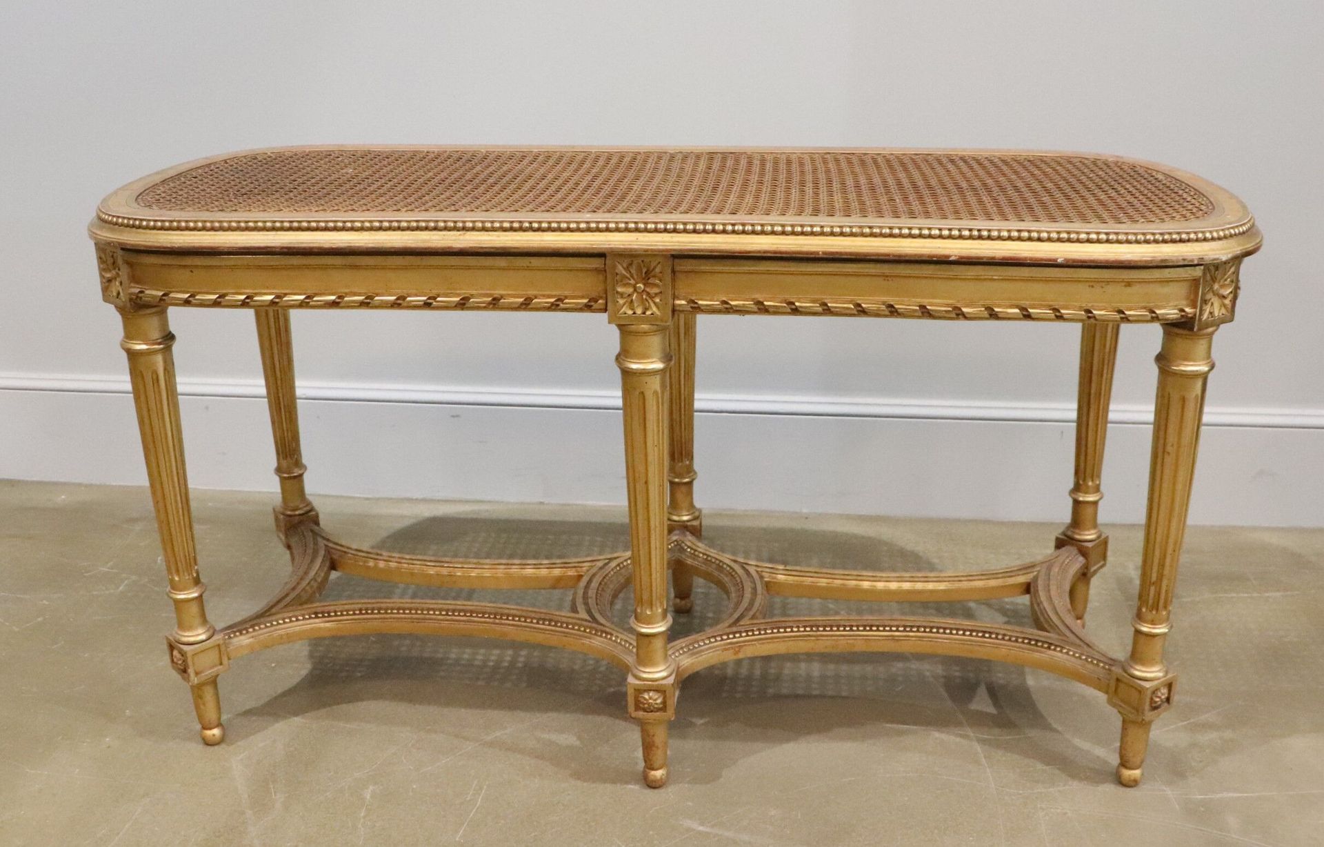 Null 镀金的木质长凳，带藤条的座位，六条腿由一个镂空的支架连接。
路易十六风格，大约.
高_50厘米，宽_96.5厘米，长_39厘米