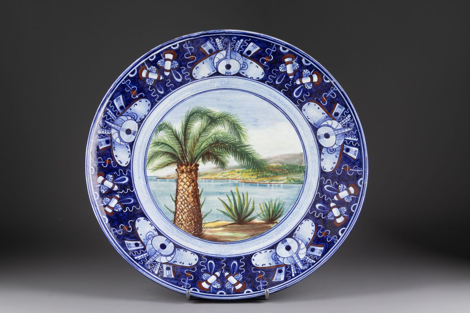 FAENZA 饰有湖景的圆盘，两翼有音乐奖杯 
多色釉陶器 
长：35厘米