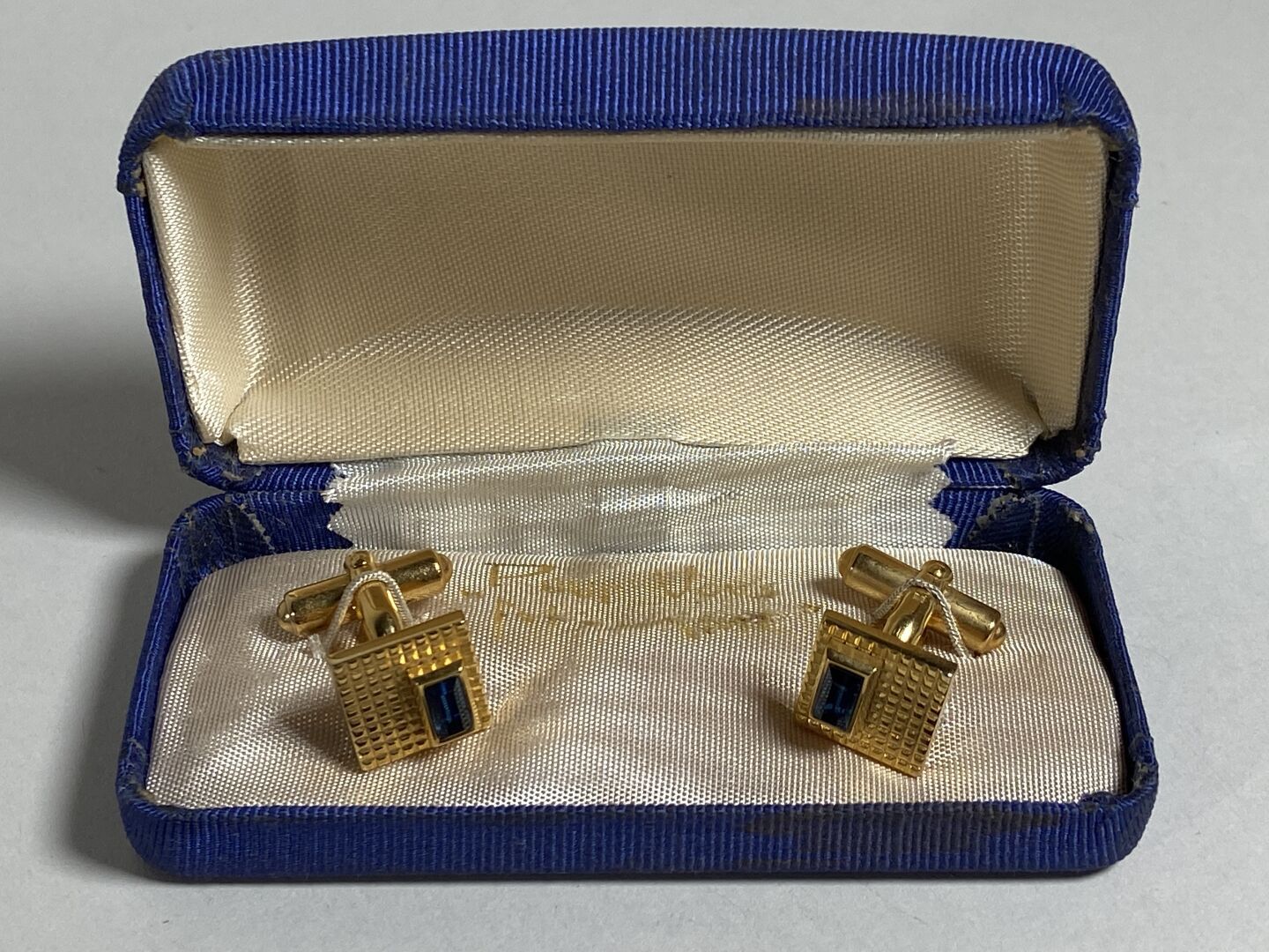 Null 一对方形扭索纹鎏金金属袖扣，镶嵌长方形切割的蓝色宝石。

呈现在原箱中。