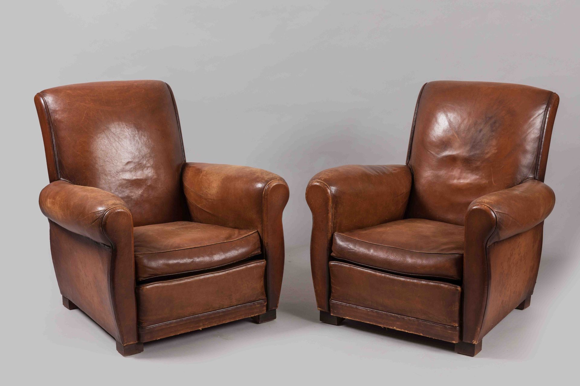Null 一对俱乐部椅子，有一个略微翻转的长方形椅背。棕色皮革内饰。它们站在四个方形的彩色木腿上。

20世纪。

高度：84厘米。宽度：79厘米。深度：53厘&hellip;