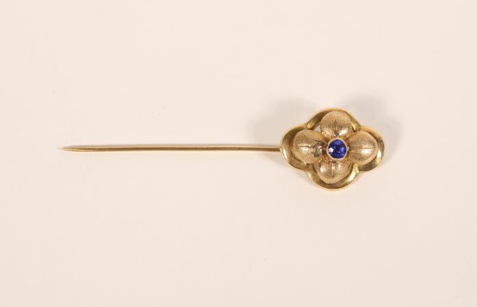 Null 750‰的18K黄金针，装饰有一朵以阿玛蒂为图案的多叶花，镶嵌有一颗蓝色宝石。
变形。
毛重：1.80克