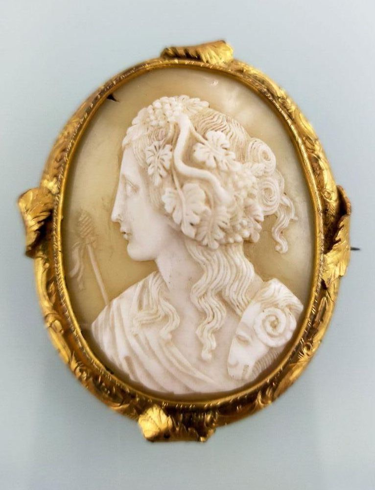 Null 黄金585千分之一的胸针，在一个浮雕贝壳的中心装饰，代表一个女人到古董的小半球的周围。
金属的销子。
(凹痕和焊接的痕迹）。
高度 : 4,4 cm
&hellip;