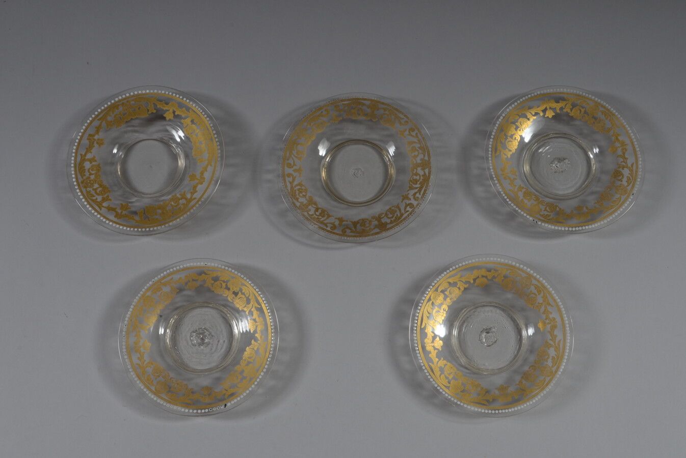 Null Cinq soucoupes en verre incolore à décor émaillé or et blanc de rinceaux.