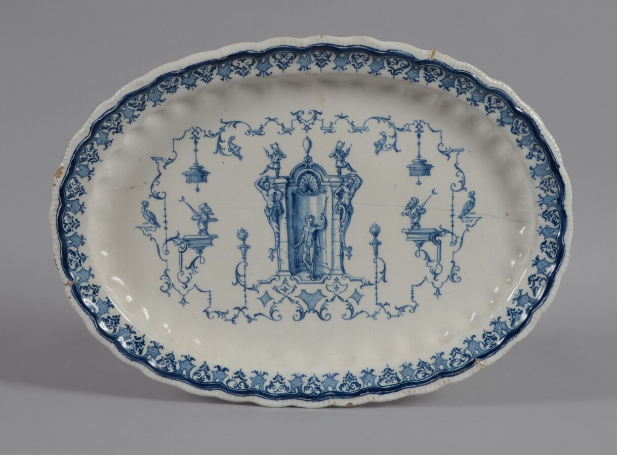 Null 搬家公司
椭圆形陶盘，边缘有锯齿，装饰有蓝色单色的 "à la bérain "和翅膀上的刺绣图案。
18世纪
长38厘米
裂缝和装订
