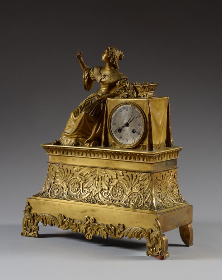 Null 一个有凹槽和鎏金的青铜钟，站在四个小脚上，正面装饰着叶子的卷轴，装饰着一个优雅的女人靠在桌子上，拿着有罗马数字的漆面金属表盘。 
19世纪 
高44 &hellip;