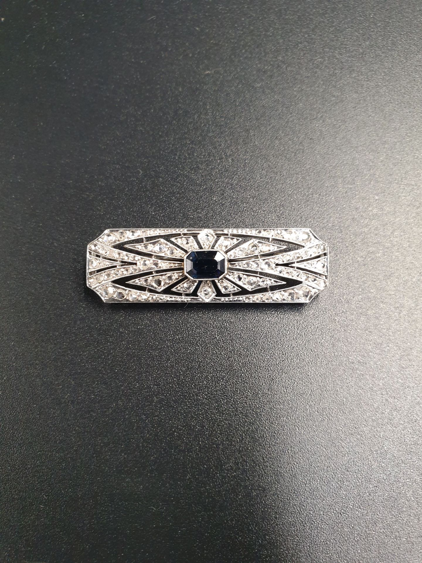 Null 装饰艺术风格的白金胸针，镶嵌着一颗刻面蓝宝石，周围有小钻石。
毛重：约6.93克。
长度约为4.5厘米