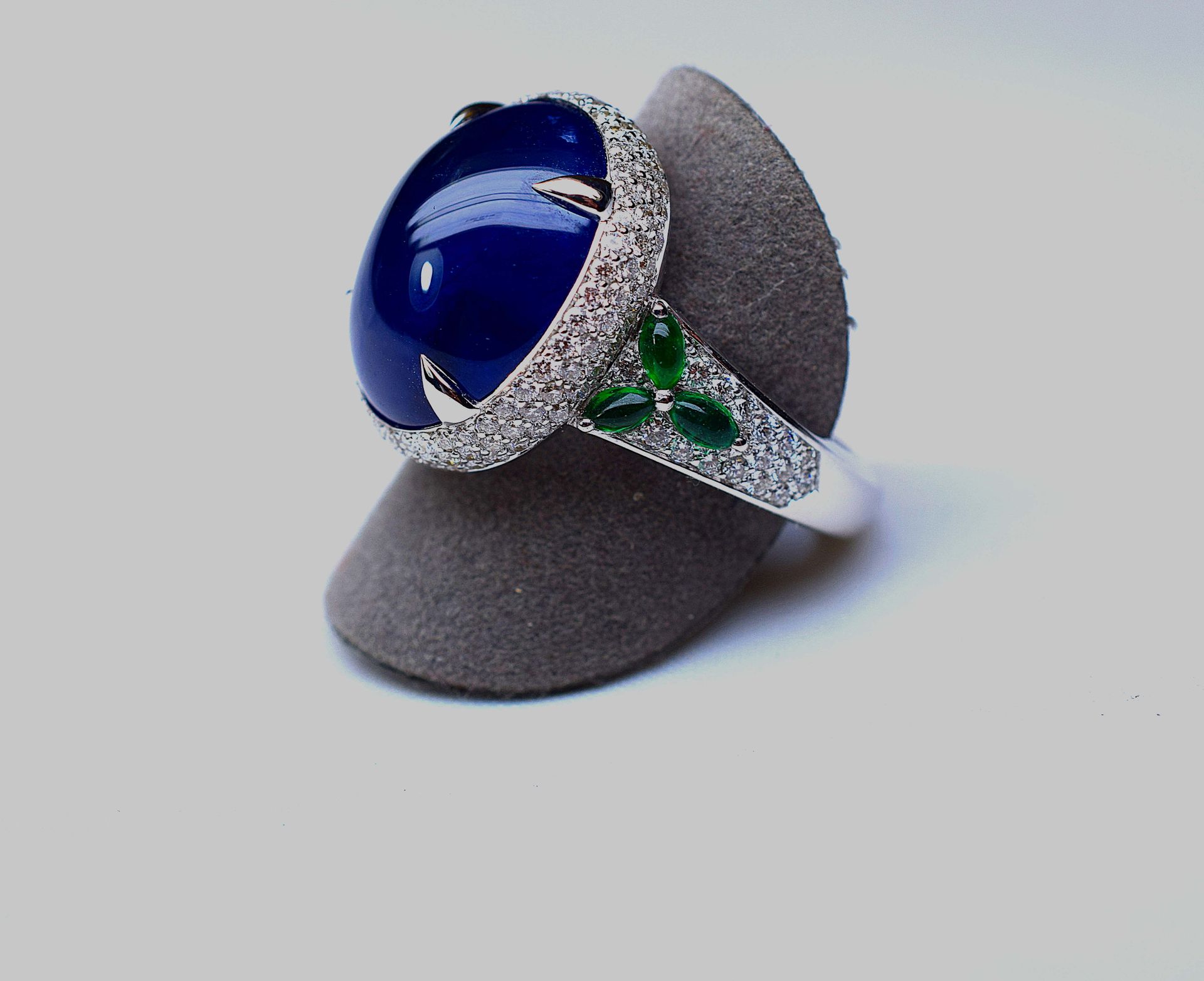 Null 白金戒指上镶嵌着一颗大型天然凸圆形蓝宝石，可能是锡兰的，重14.69克拉。 镶嵌着现代切割的圆钻和6颗天然榄尖形祖母绿，重约2克拉。黄金8.77克。这&hellip;