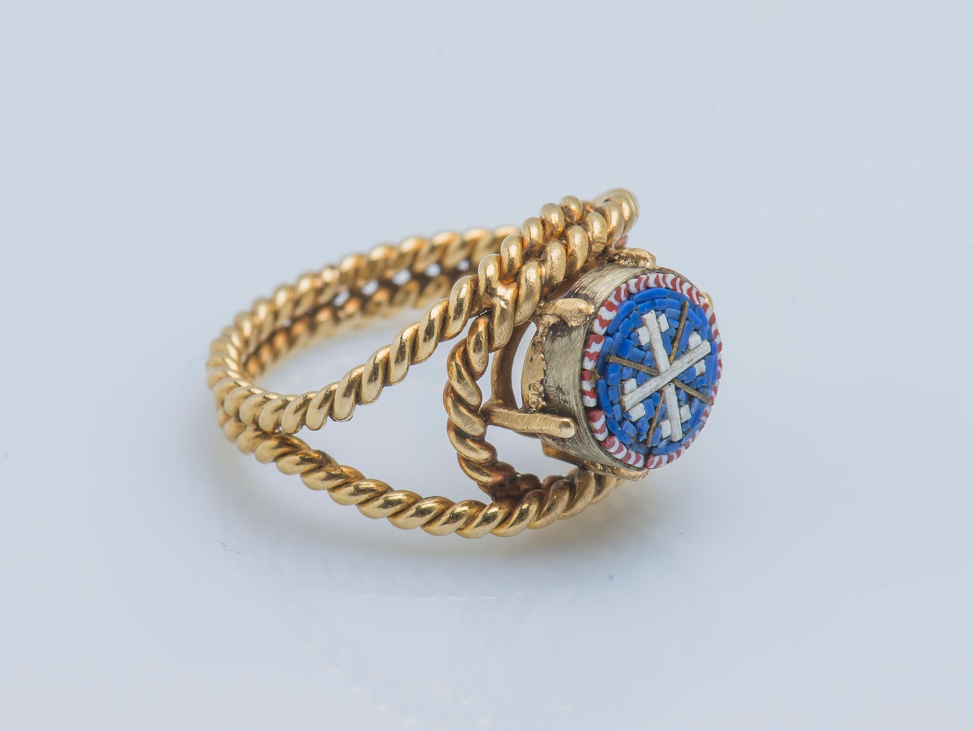 Bague 
一枚18K黄金（750‰）和银（850‰）的戒指，形成一个双绳装饰的带子，镶嵌着一个圆形的微马赛克，描绘着蓝底的有力十字架。
手指大小：45 毛重&hellip;