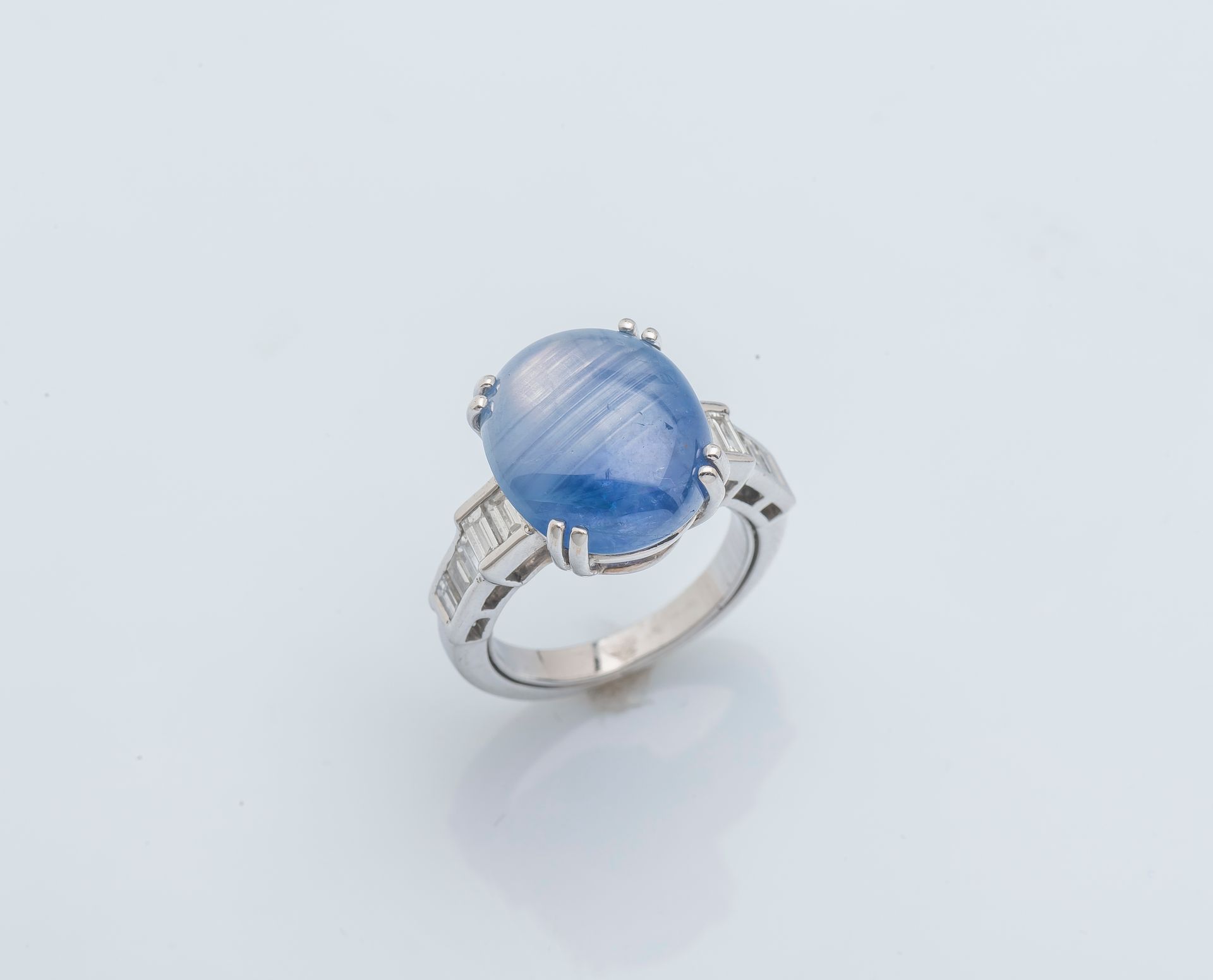 Null 一枚18K（750‰）白金戒指，镶嵌着一颗凸圆形的星形蓝宝石，重约9.7克拉，戒指的肩部镶嵌着层层叠叠的祖母绿切割钻石。法国的工作。

手指大小：47&hellip;