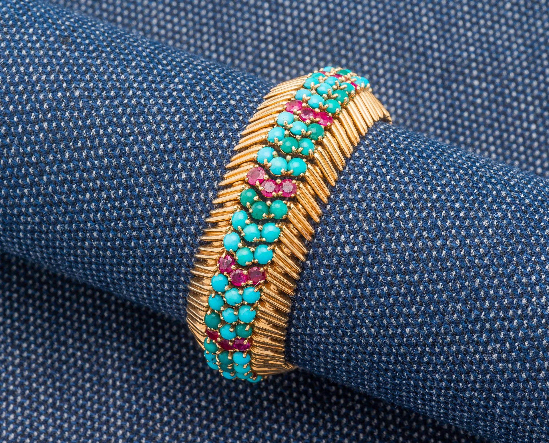 Null 一条18K黄金（750‰）的弧形丝带手镯，在两排金钉之间装饰有圆形绿松石和凸圆形红宝石。法国的工作。

长度：16.5厘米 毛重：87.8克