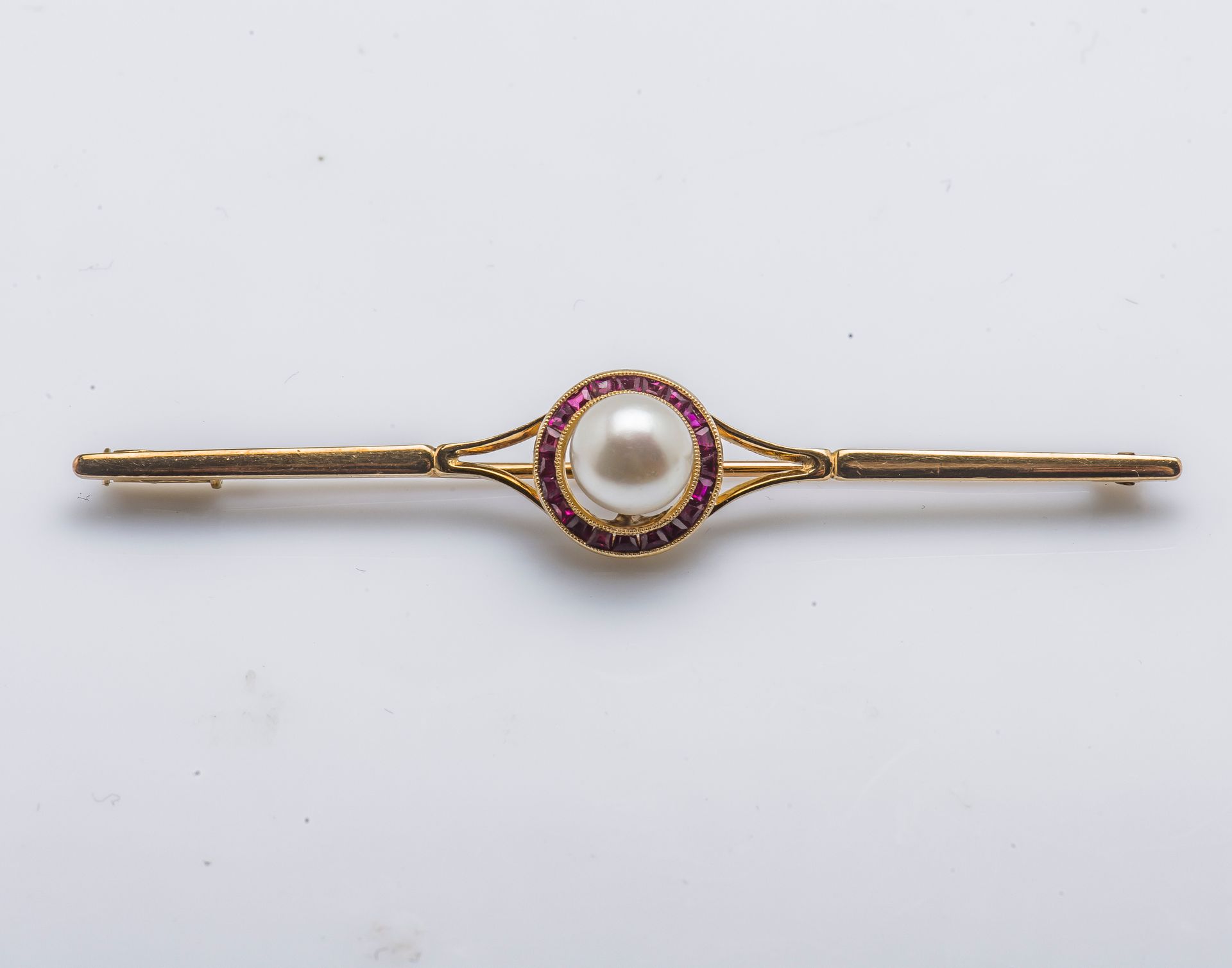 Null 一枚18K（750‰）黄金发夹胸针，在校准的红宝石周围镶嵌了一颗纽扣养殖珍珠。法国的工作。

宽度 : 6,7 cm 毛重 : 4,5 g