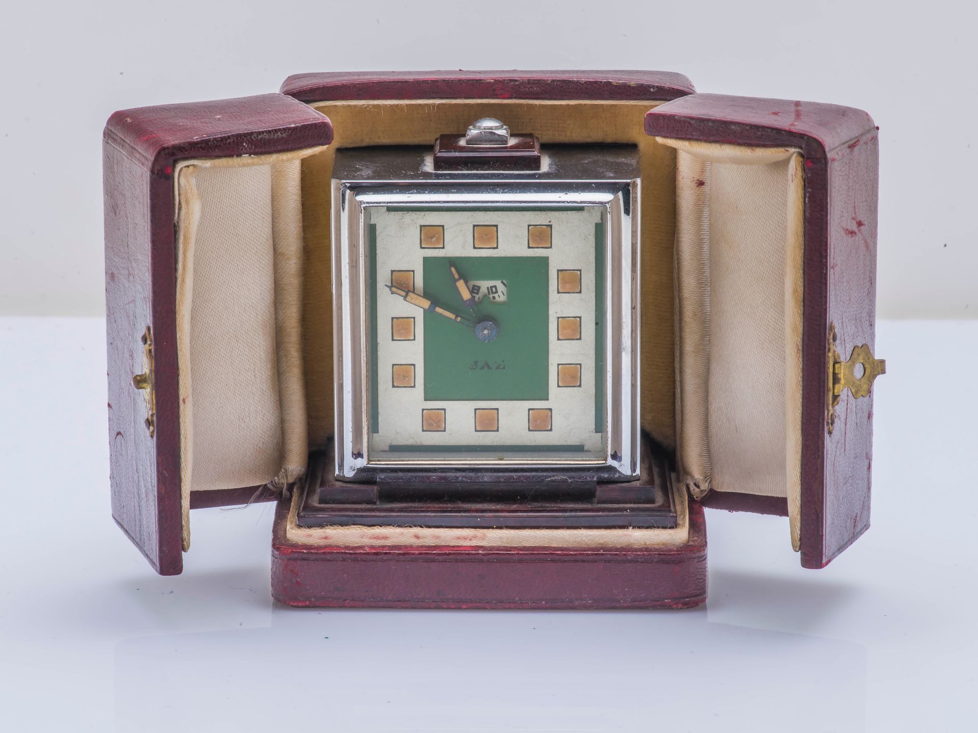 JAZ vers 1930 JAZ约1930年

银色金属旅行闹钟，方形，在仿木质的电木底座上，奶油色和绿色的表盘上有方形的发光指示器，12点钟位置有闹钟时间窗&hellip;