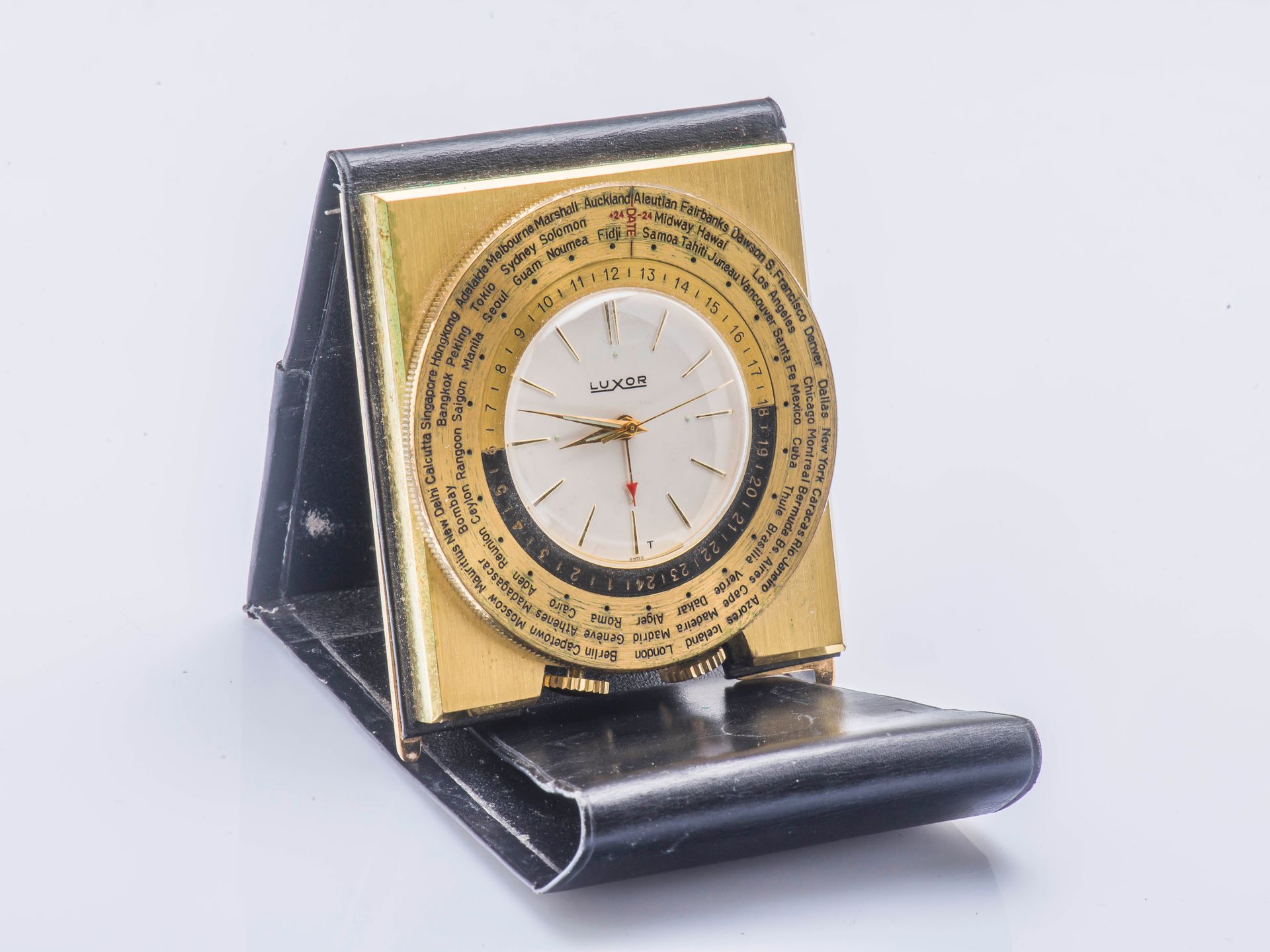 LUXOR vers 1960 世界时间旅行钟，具有闹钟功能和世界时间。鎏金黄铜方形，装在黑色皮箱中。银色表盘上有应用金质指数、秒针和标有红色箭头的闹钟指针。旋&hellip;