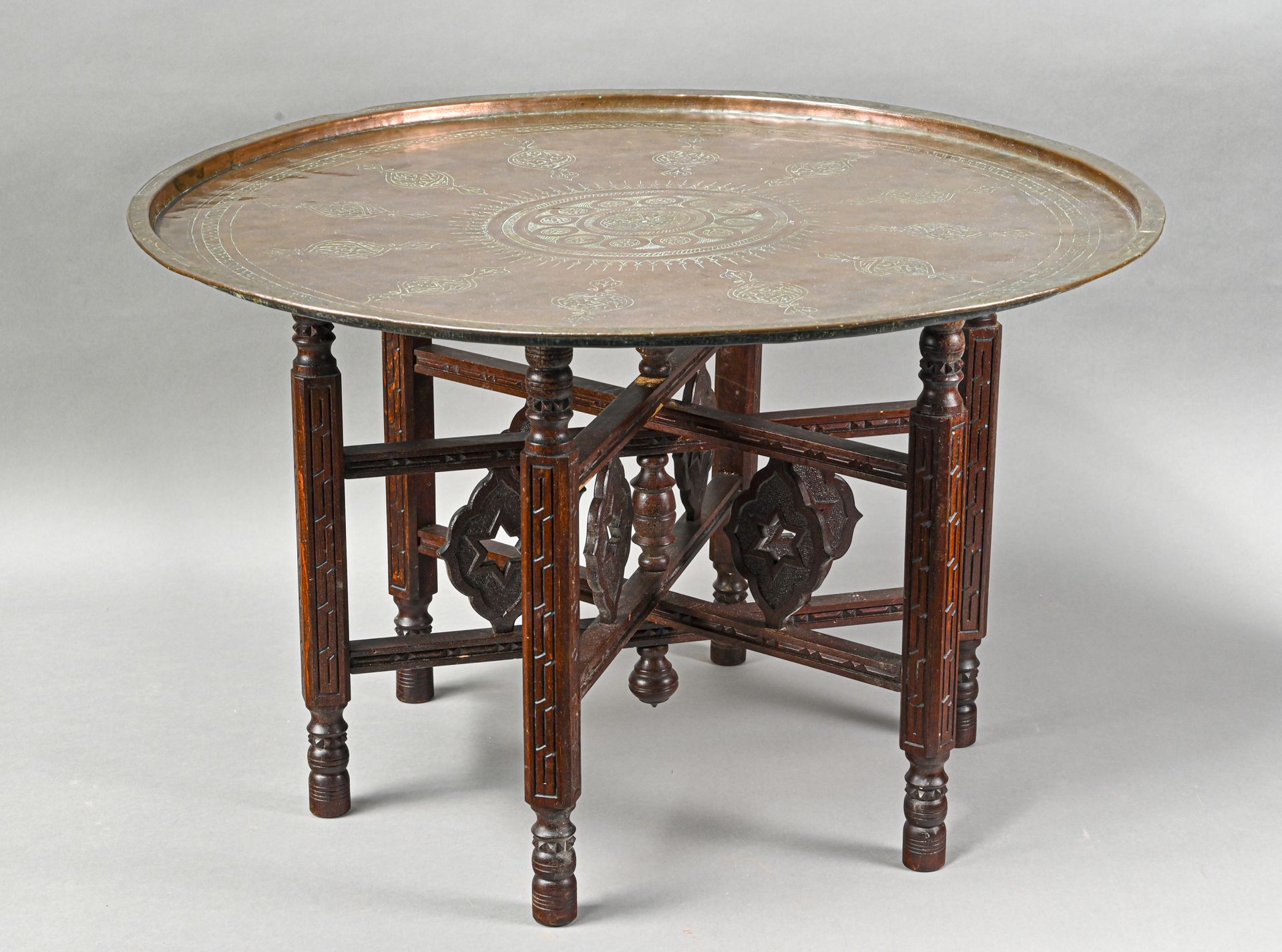 Table à thé 由一个雕刻的铜制顶部和一个有六条腿的雕刻的木制铰接式底座组成，装饰有镂空的星星

H.47 cm - D. 77 cm

凹痕和磨损