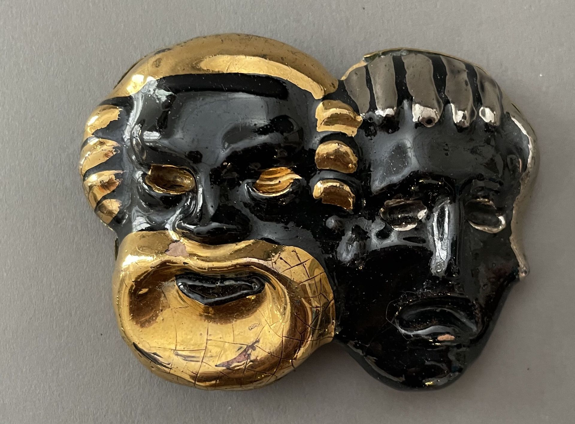 Null 高级时装的陶瓷皮带扣，约1940年，黑色、金色和银色的釉面陶瓷扣，带有仿古面具装饰，安装在鎏金铜板上，（2个缺口），6.3 x 8厘米。 

拍卖品可&hellip;