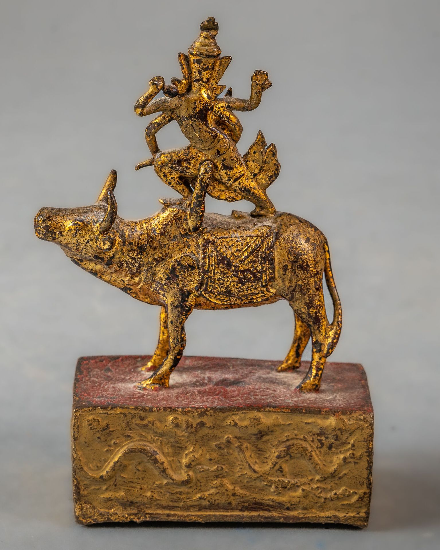 Null 黄金和红漆青铜小雕塑，泰国，19 世纪末
雕像表现湿婆神，四臂抱着各种属性，站在他的坐骑水牛上，水牛栖息在饰有两条蛇的长方形底座上。已磨损
H.14.&hellip;