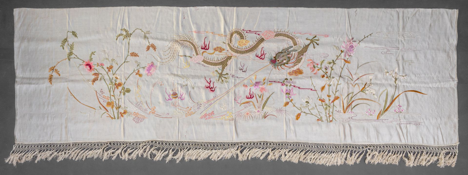 Null 刺绣白丝披肩，印度支那，越南，20 世纪早期
多彩装饰（粉色）：一条龙在各种花朵间追逐一颗珍珠，一侧有流苏。
小污点
H.34 厘米 - 2.4 米宽