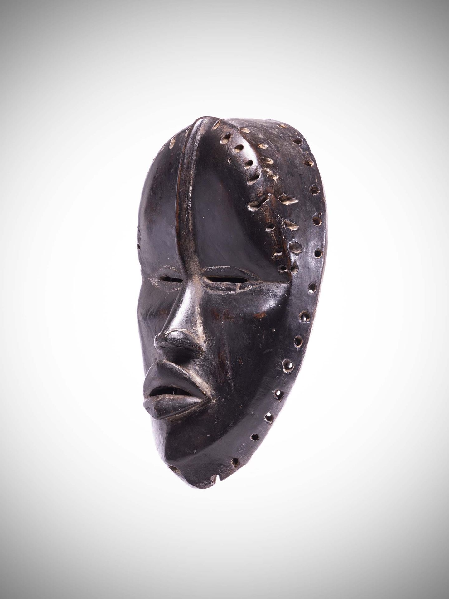 Null 丹

(象牙海岸) 非常优雅的面具，有黑色的漆面光泽。

浮雕式的额脊延伸了鼻子。

用双排孔来连接头饰和布衣。

沉重的木材。高度：21.5厘米