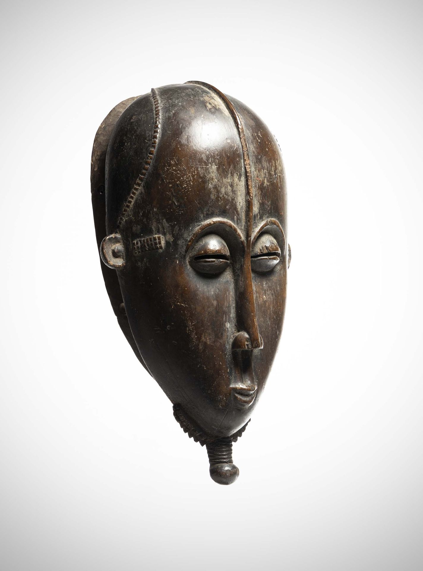 Null Yaouré

(象牙海岸)优雅的男性面具由厚重的木头制成，有使用后的铜锈。

细长的鼻子在浮雕中被垂直的额脊延长了。

在下巴的底部雕刻了一个辫子状&hellip;