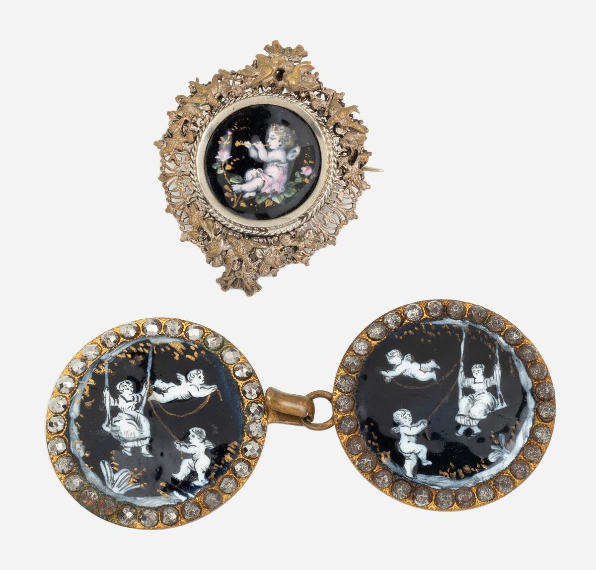 Null 一套三个银色或铜色金属上的珐琅小品，包括一个服装上的双缝夹，上面有格子图案的小品，还有一个珐琅胸针，上面有一个天使在燕子的框架中吹笛子。这个19世纪末&hellip;