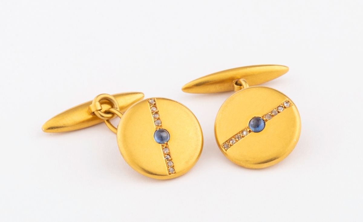 Null 18K黄金（千分之七十五）圆形袖扣，由一排玫瑰式切割钻石交叉而成，中间是一颗浅蓝色凸圆形蓝宝石。 
直径：1.5厘米。 
毛重：7.3克。