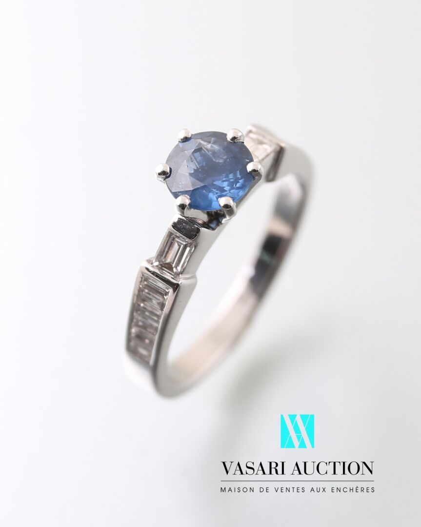 Null 白金戒指750千分之一，中央镶嵌一颗圆形切割蓝宝石，约1克拉，由长方形切割钻石支撑。

毛重：4.75克 - 手指尺寸：54