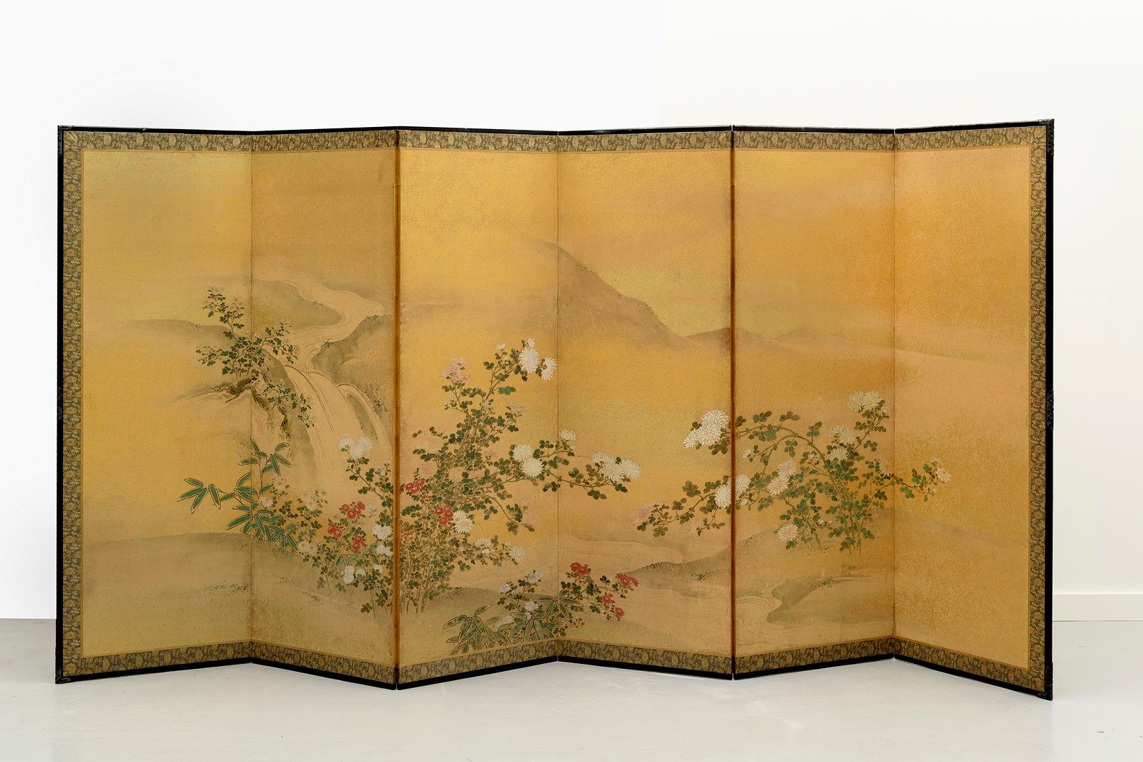 Null 日本，明治时期（1868-1912）。一幅大型的Rimpa风格的六叶byobu屏风，在金色的斑点纸上用彩色绘制，在溪流两岸的菊花丛中形成瀑布，山脉的剪&hellip;
