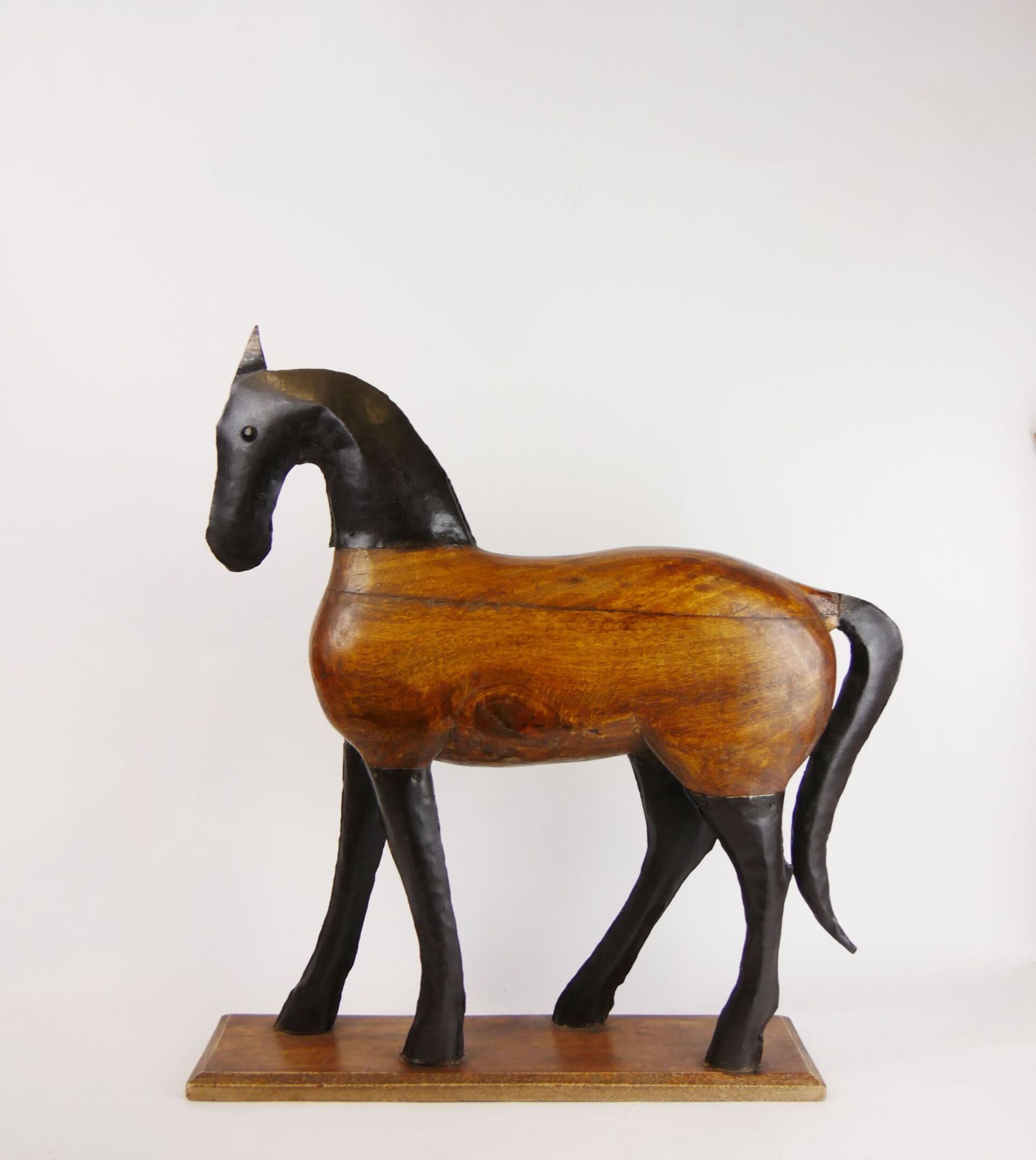 Null Pferd aus geschnitztem Holz und schwarz bemaltem Metall, das auf einer rech&hellip;