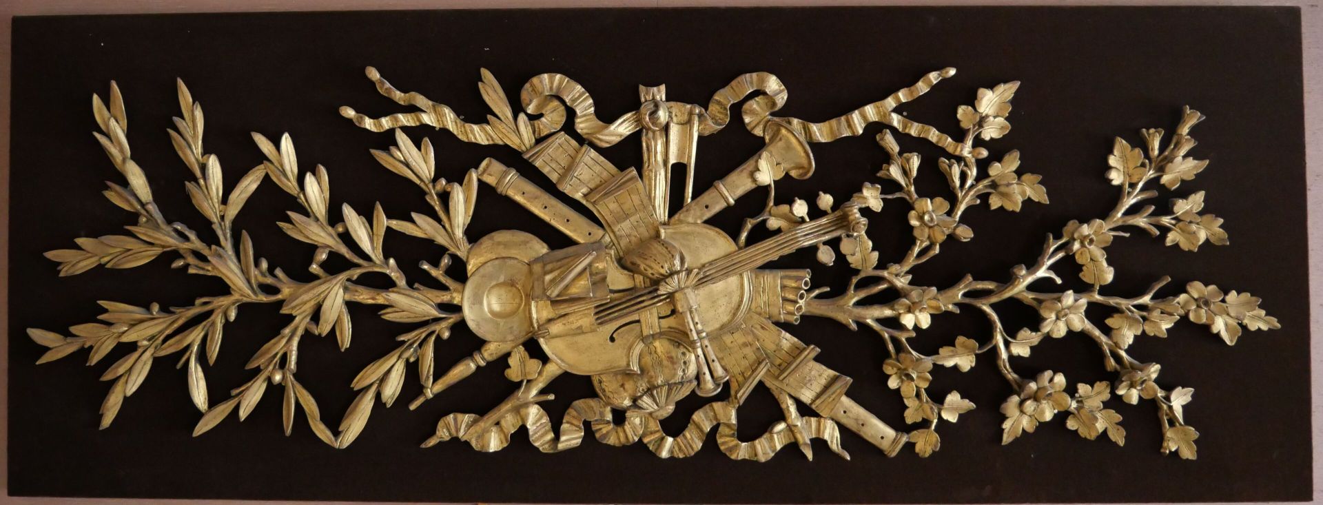 Null 两件雕刻和镀金的木制装饰品，代表了月桂树、橄榄树和丝带蝴蝶结背景下的乐器战利品。 
(长方形的棕色天鹅绒支架）。 
尺寸：55 x 147厘米 

专&hellip;