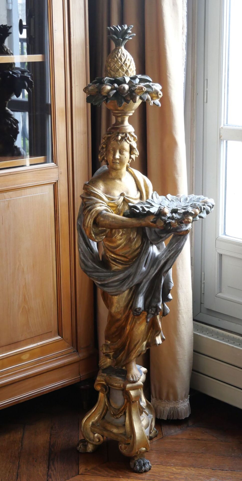 Null 一个多色，镀金和银色的木雕茶灯架，表现了一个年轻女子披着古色古香的衣服，站在一个三角形的底座上，上面有一个叶子的杯子，头上支撑着一个菠萝。爪形脚。
路&hellip;