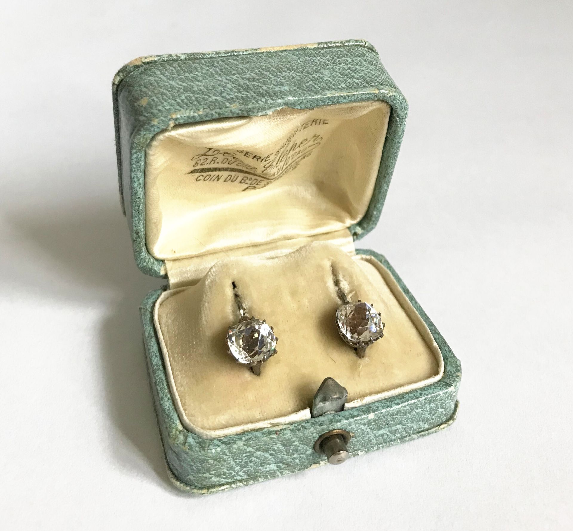 Null 一对花式 "卧蚕 "耳环，金属支架上镶嵌着仿制钻石的白色石头。20世纪初
装在一个箱子里