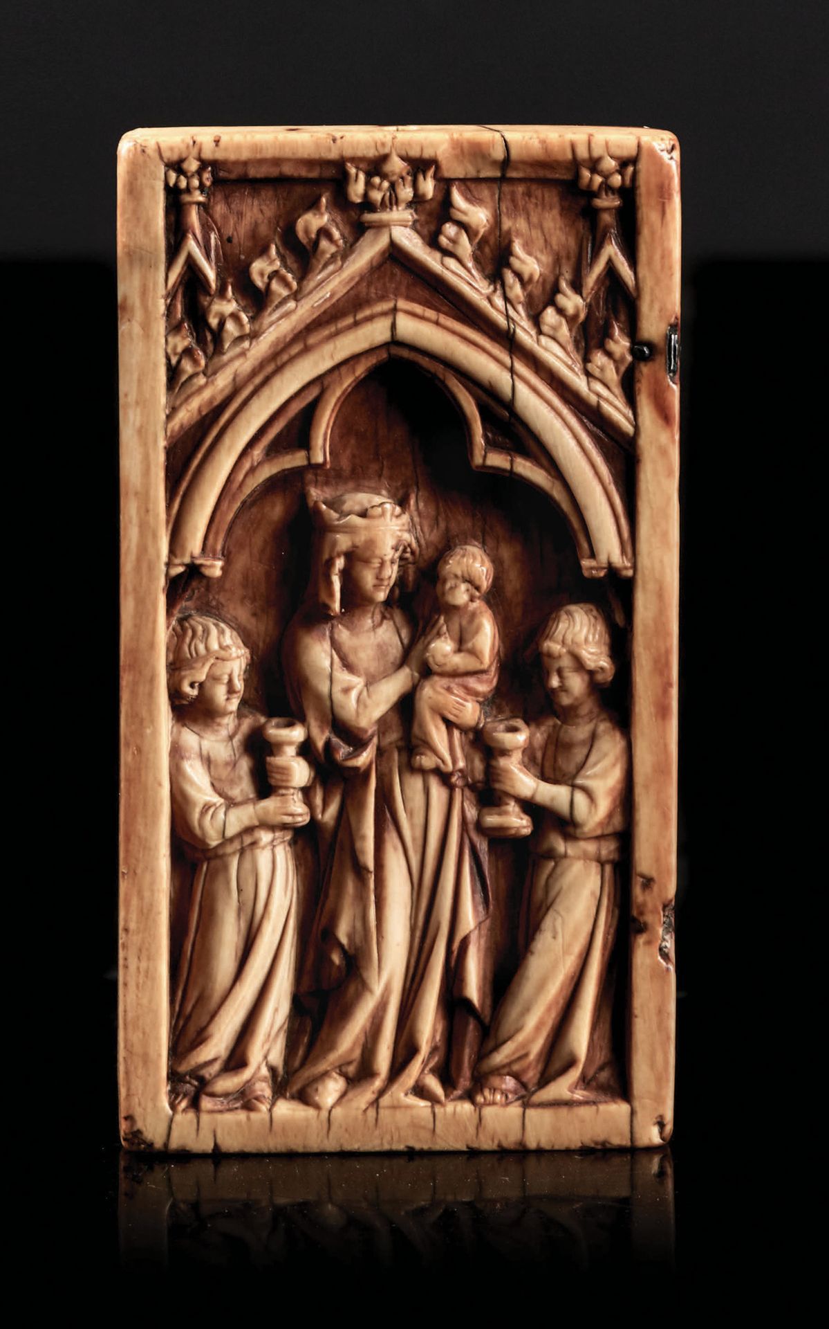 Null 浮雕象牙二联画的左页，描绘了在一个破损的拱门下的光荣的圣母，拱门上有一个带钩子、顶盖和尖顶的屋檐。头戴王冠的玛丽亚将孩子放在她的左侧；她被两个手持烛台&hellip;