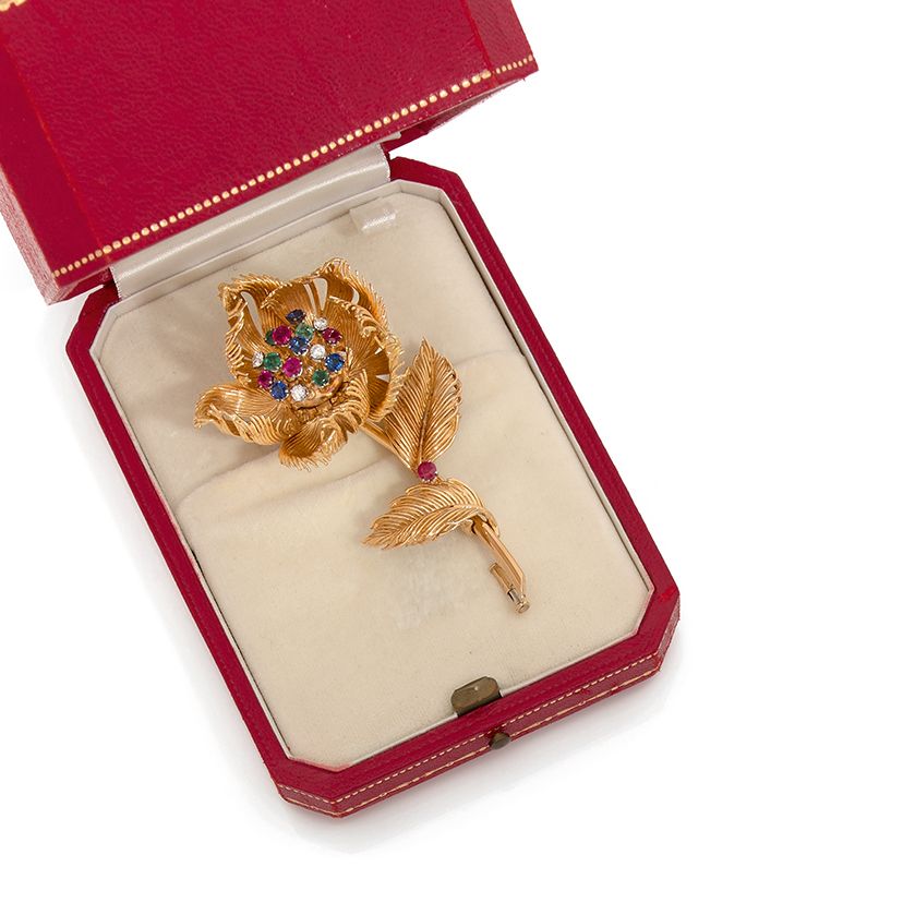 CARTIER 18K(750)金线胸针夹，造型为铰接式花瓣的玫瑰。花蕊上镶嵌着明亮式切割钻石、蓝宝石、绿宝石和圆形刻面红宝石。
有签名和编号的016785。
&hellip;