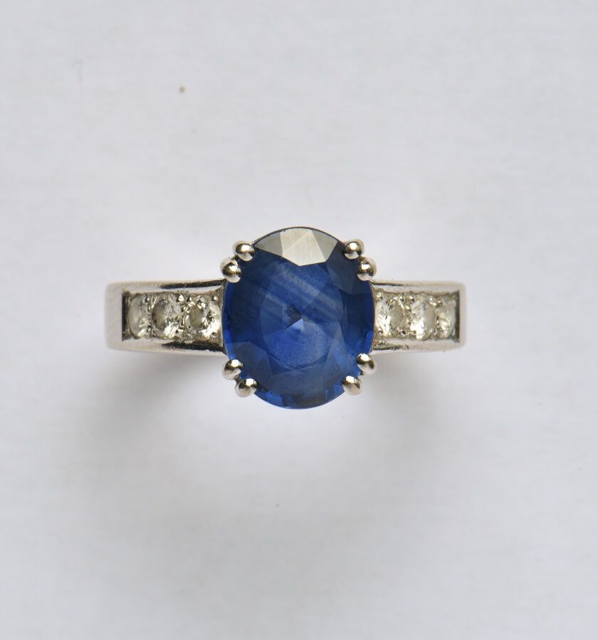 Null 18K（750/oo）白金戒指，以一颗重约3.30克拉的椭圆形蓝宝石（可能经过热处理）为中心，镶嵌着一排明亮式切割钻石。TDD 54。毛重：6.4克。