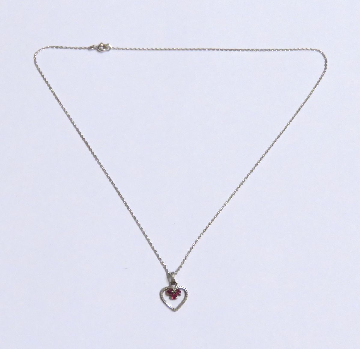 Null 18K白金 "心 "形吊坠，镶嵌三颗小型明亮式切割红宝石。18K白金链上有精美的 "forçat "链接。 总毛重：2克45。链条长度：38.5厘米。