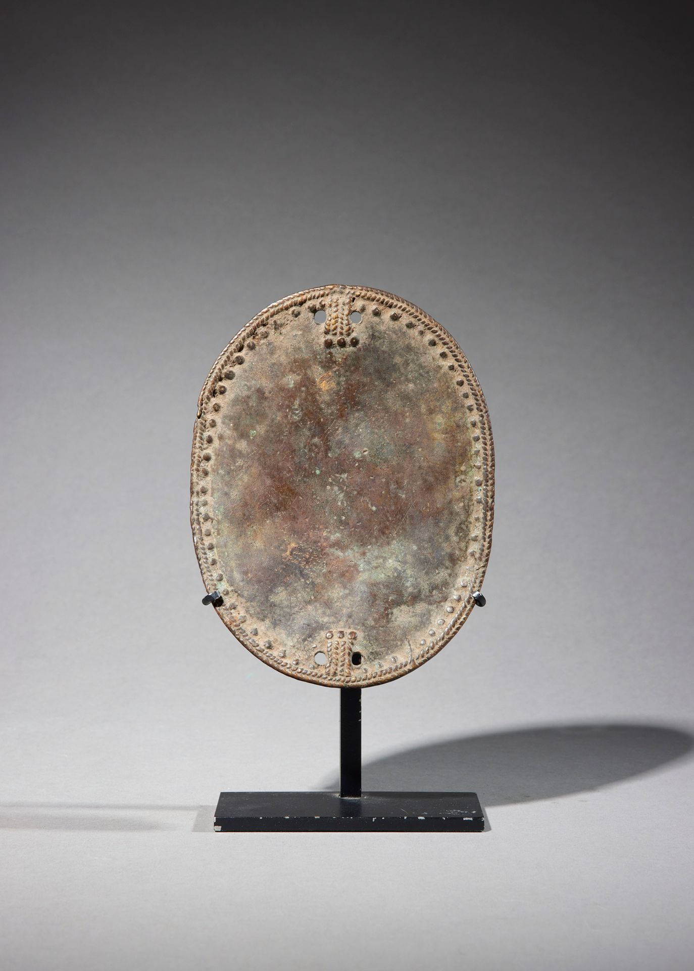 Null 装饰板

西非

铜质

H.15.1厘米



椭圆形的装饰盘，装饰有双辫子门楣和一连串的浮雕点。四个固定点被刺穿。