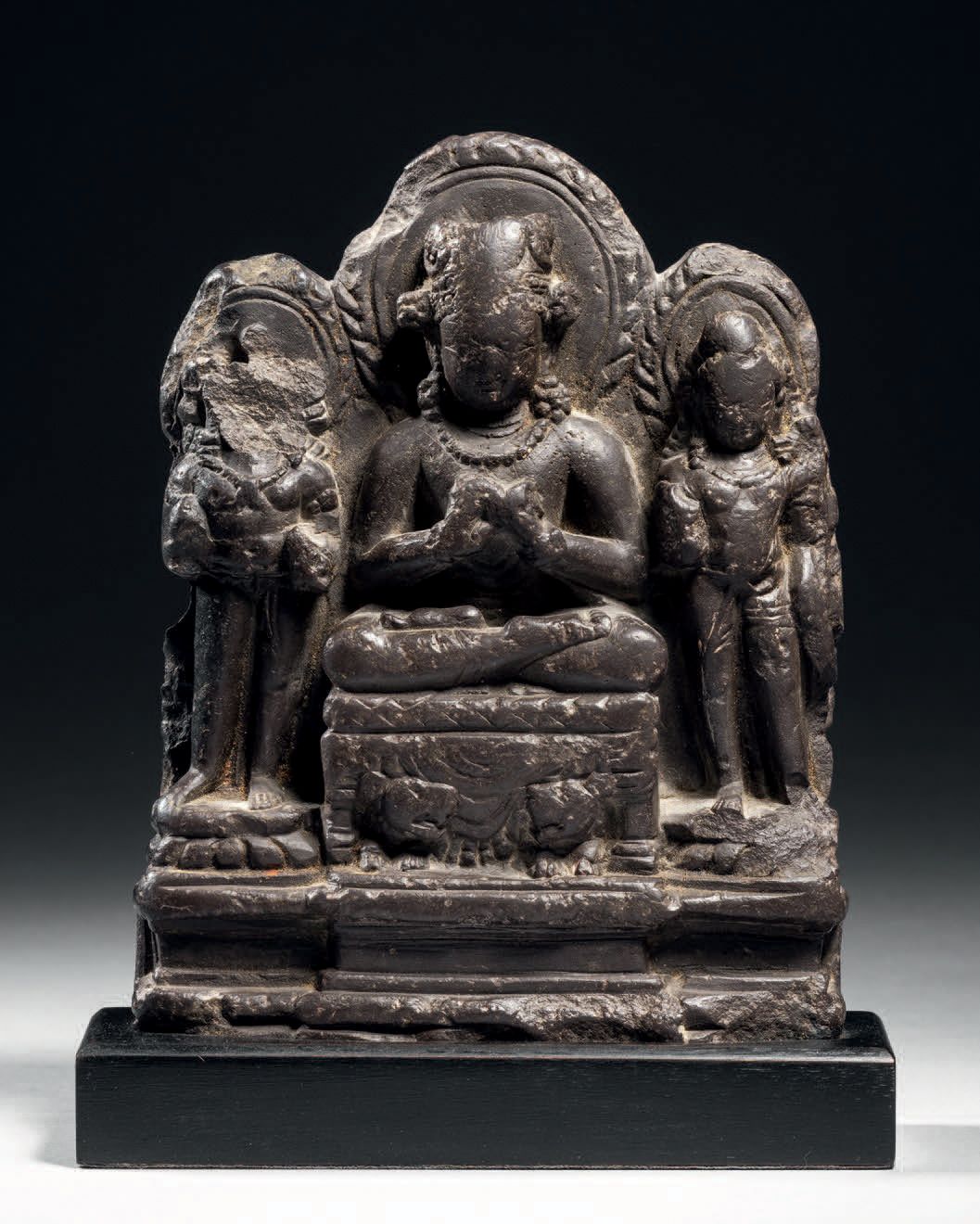 Null 印度克什米尔，8世纪，高14厘米。灰色绿泥石
被装饰的佛陀做出了坐在宝座上传教的姿态，宝座上有两只狮子在相互对视。他戴着一条项链和珍珠耳环。两位菩萨站&hellip;