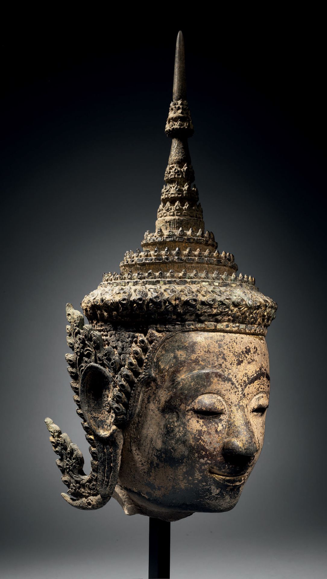 Null 佛教侍者头像，泰国大城府风格，18世纪，高41厘米。多色砂岩和铜合金
神灵的脸是微笑的，半闭着杏仁形的眼睛，合拢的嘴唇升到嘴角，眉毛上扬。头饰让人联想&hellip;