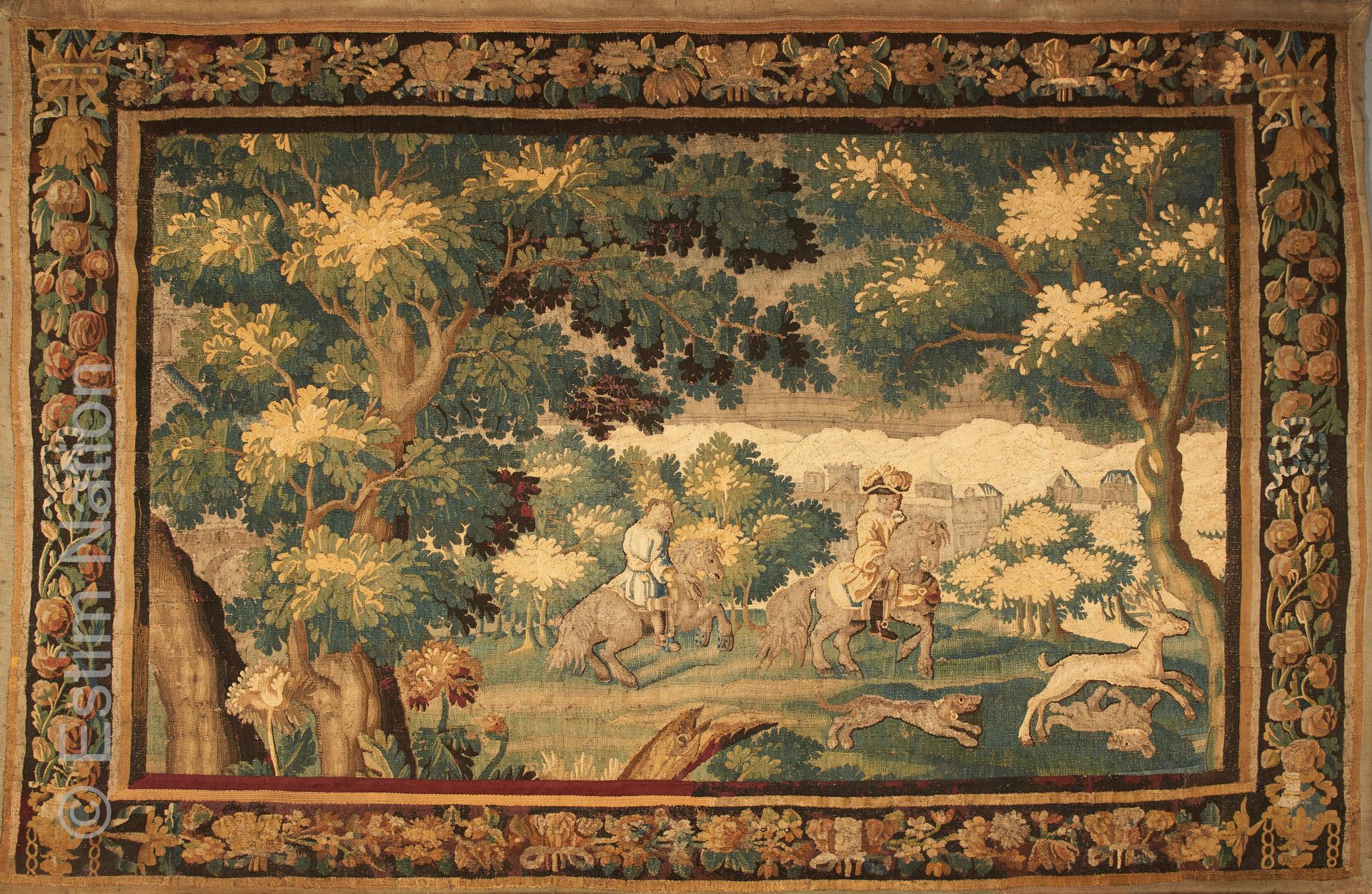 AUBUSSON 被称为 "verdure "的多色羊毛挂毯，装饰着一个狩猎场景，画面上有两个骑手和他们的狗在跟踪一只鹿，背景是一座城堡，丰富的边框和棕色背景上&hellip;
