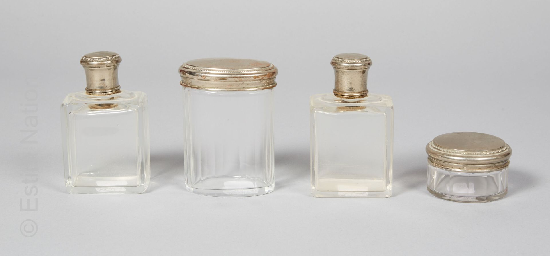 MÉTAL ARGENTÉ 模制玻璃洗漱用品套装，镀银金属框架，装饰有珍珠楣。它包括两个长方形的瓶子和两个有盖的盒子，一个是椭圆形的，一个是有切边的圆形。


&hellip;