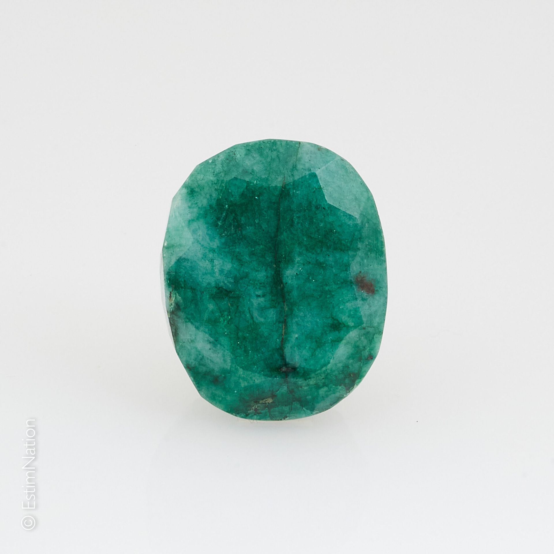 UNE ÉMERAUDE SUR PAPIER ET EXAMEN A large emerald on paper of faceted oval shape&hellip;