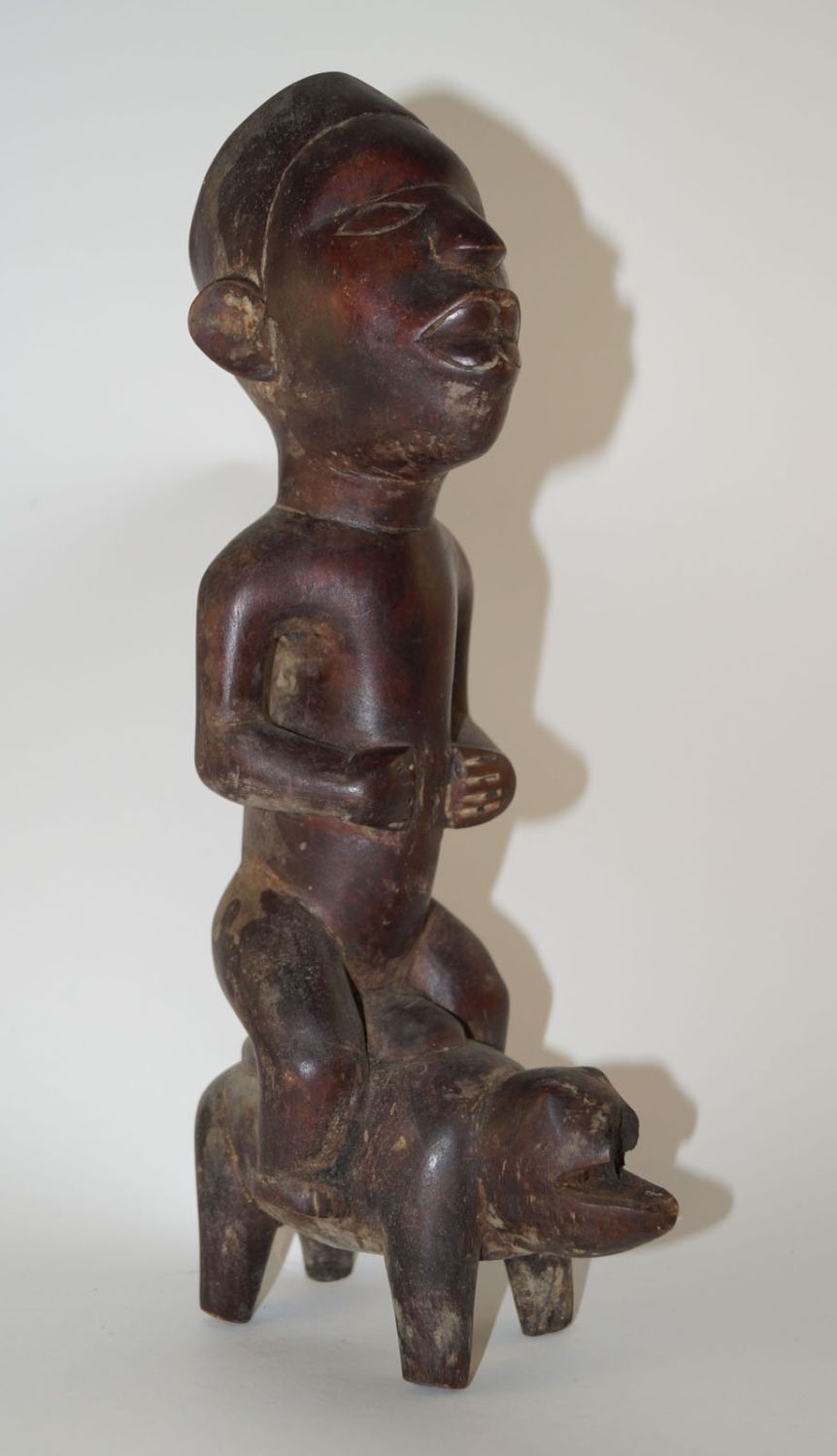Afrika,Statue, In DR Kongo Stil 高31厘米。坐在猪身上的男性形象，面部雕刻得非常精细。厚重的带红色的木头，带有闪亮的红色铜锈。 &hellip;