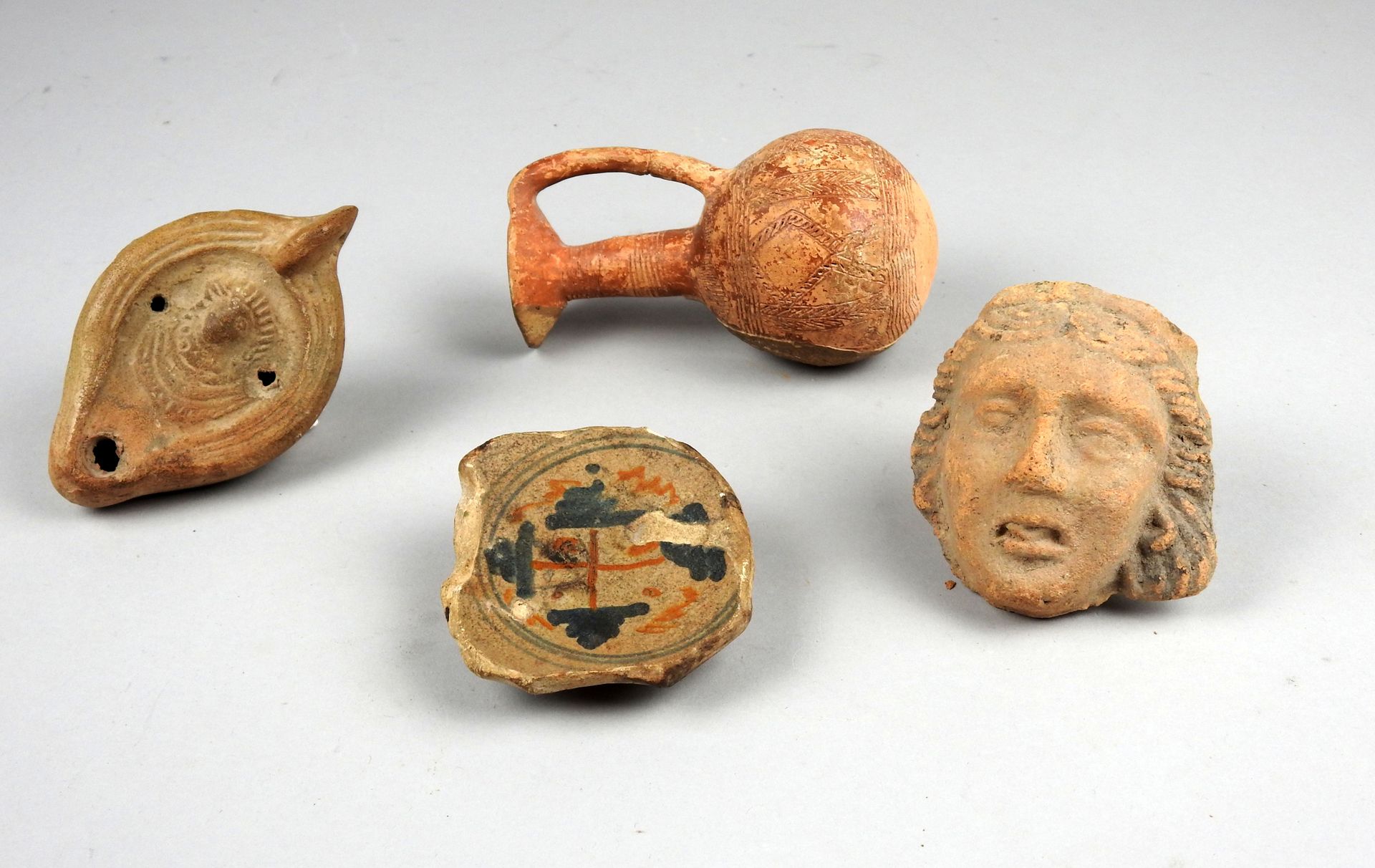 Null 一套四件物品，包括一个女性面孔，一个有十字架装饰的花瓶底座，一个有面孔的油灯，和一个有刻字几何装饰的花瓶

陶器7.5至11厘米

古代和后来的世界