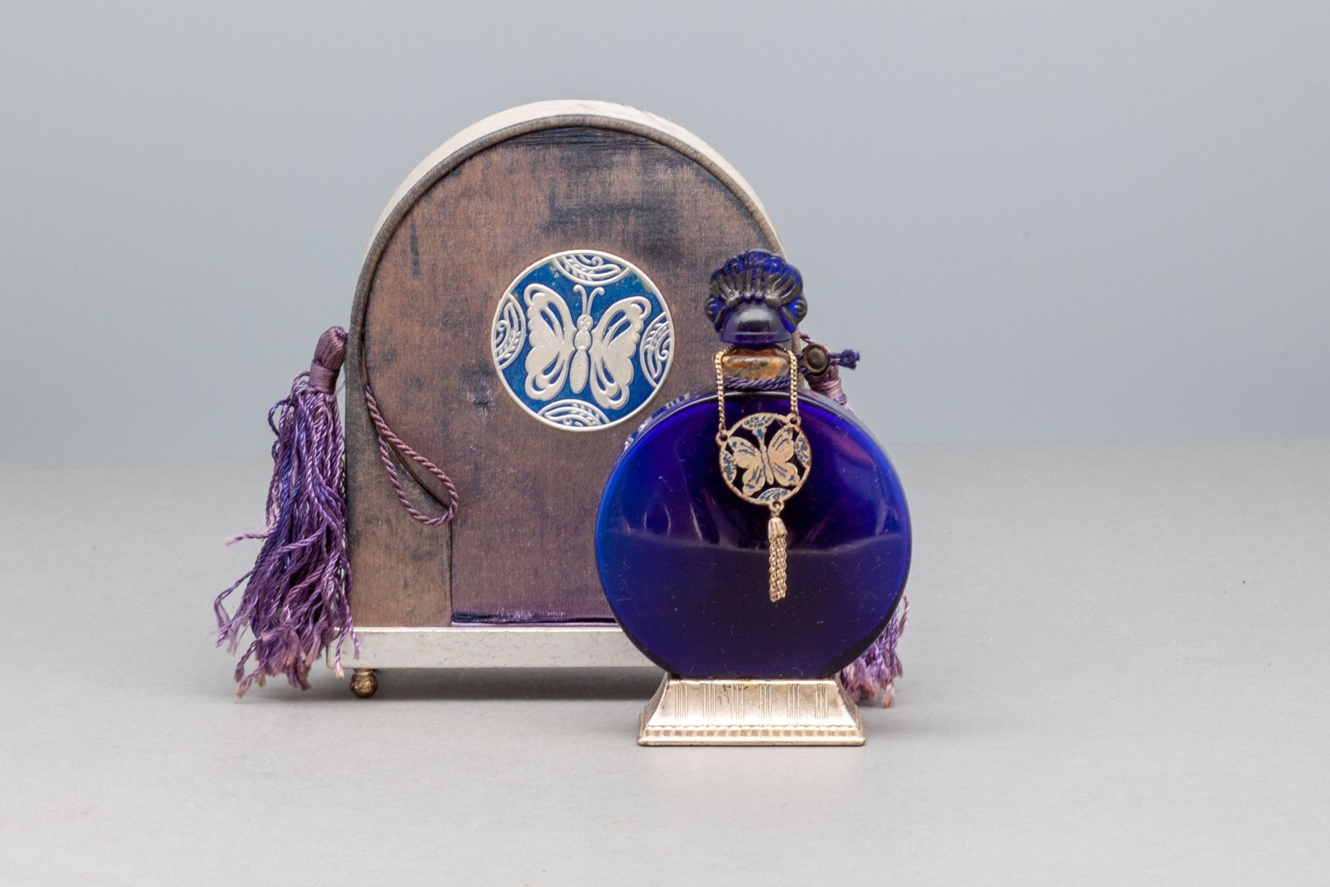 LUCRETIA VANDERBILT 蓝色玻璃瓶，装饰有流苏的蝴蝶。有标题的金属底座。缎面包覆的箱子两侧是吊坠。高瓶10.2厘米 - 高箱12.3厘米