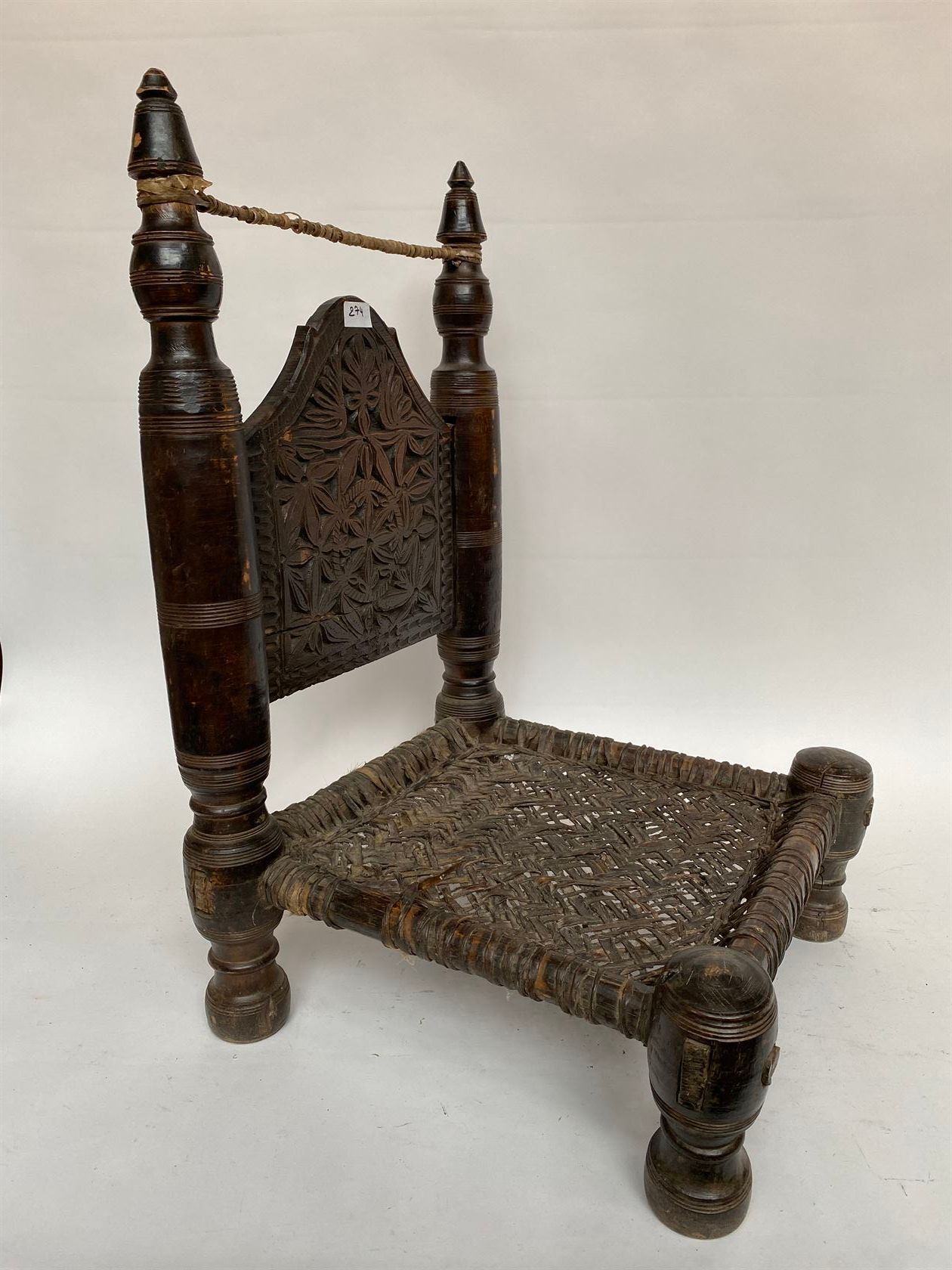 Null 两把低矮的椅子放在四条翻转的木腿上，栏杆式的立柱，椅背上雕刻着花和叶子，座椅用皮革编织而成。阿富汗。靠背高度为82和76厘米。